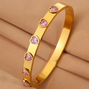 Détail d'un bracelet doré orné de zircons roses en forme de cœur sur tissu beige