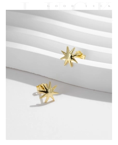 Detailed view of gold sunburst star stud earrings on a white minimalist backdrop