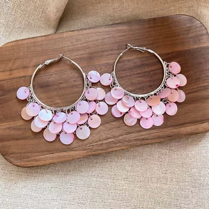 Detail of silver hoop earrings with tiered pink shell pendants on rustic linen cloth