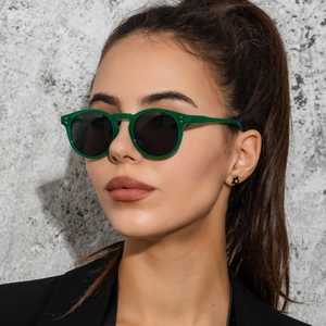 Close-up of green vintage sunglasses with black lenses worn by a model in a fashion shot