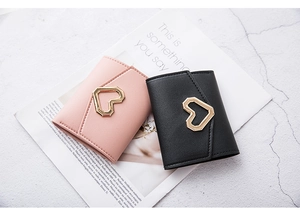 Detail of pink and black heart lock wallets with litchi grain texture on white desk
