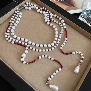 Macro detail of vintage multi-layer pearl necklace with red beads on velvet tray