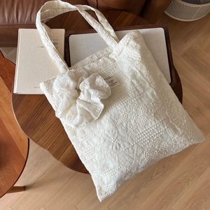 Detail of white lace embroidered tote bag with a large bow on a rustic wooden table