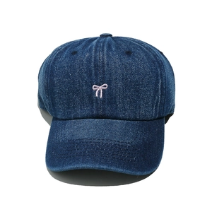 Close-up of pink bow embroidery on dark blue denim baseball cap with fine fabric texture