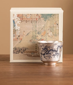 Detalle de taza de té plateada con motivo de dragón y elegante caja de regalo de lujo