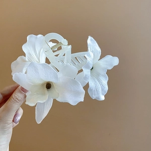 Close-up of white fabric orchid floral hair clip with cream acrylic jaw and gold metal spring