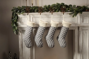 Detail von vier grauen Strick-Weihnachtssocken mit Rautenmuster, die am Kamin hängen