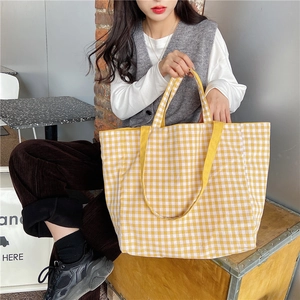 Close-up of yellow checkered canvas tote bag held by a model in a cozy indoor setting
