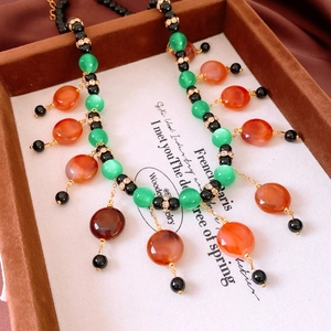 Detail of vintage beaded necklace featuring green cat eye stones and red agate charms