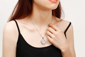 Detailed view of silver heart-shaped relief on a round pendant worn by a model