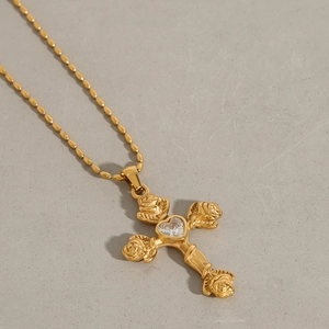 Détail du pendentif croix dorée avec roses sculptées et zircon en forme de coeur