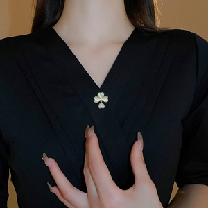 Detail of clover brooch with heart charm on a black V-neck garment, elegant gold finish