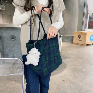 Detail of dark green plaid tote bag with cute white plush sheep charm accessory