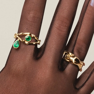 Artistic gold-plated twig rings with emerald green drop gemstones on model's hand