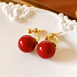 Close-up of vintage red pearl earrings with gold plating on a white embossed surface