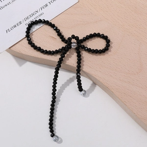 Detail of a handmade black beaded bow charm with faceted beads on a wood surface