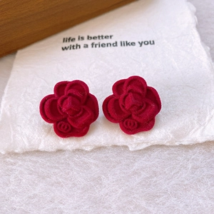 Gros plan de boucles d'oreilles camélia floquées rouge foncé sur une carte vintage