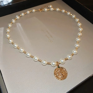 Nahaufnahme der Perlenkette mit einem goldenen Münzanhänger und grünem Edelsteinakzent