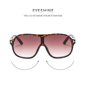 Detail of tortoise shell sunglasses featuring a golden T-shaped metal logo on the temple