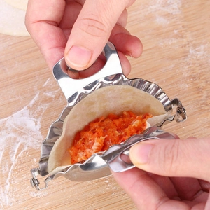 Close-up of stainless steel dumpling maker folding dough with filling on wooden board