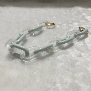 Detail of mint green and frosted acrylic link chain with golden metal rings on plush background