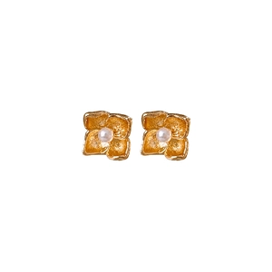 Golden flower stud earrings with central pearl on a minimalist white background