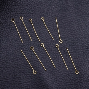 Golden stainless steel eye pins for jewelry making scattered on black leather background