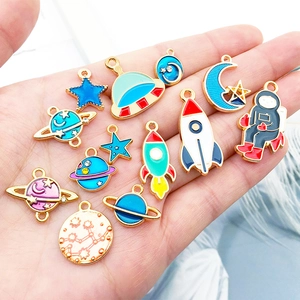 Space astronaut enamel charms set with stars and rockets held in hand for scale