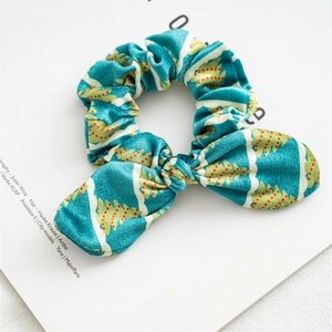 Close-up of teal Christmas velvet scrunchie with tree patterns and a cute bow detail