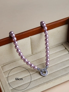 Detail of 44cm purple pearl necklace featuring silver cubic zirconia ring clasp on wood