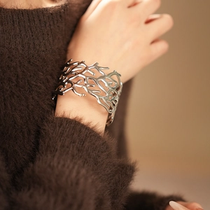 Macro detail of silver hollow cuff bracelet with coral branch texture on a soft sweater sleeve