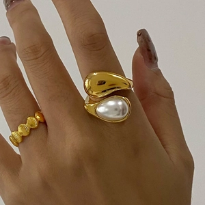 Dettaglio anello a goccia dorato con perla bianca e trama a conchiglia rifinita