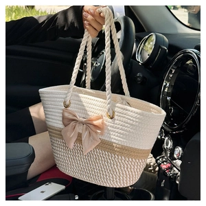 Detailed shot of a beige woven tote bag with a champagne bow held inside a car