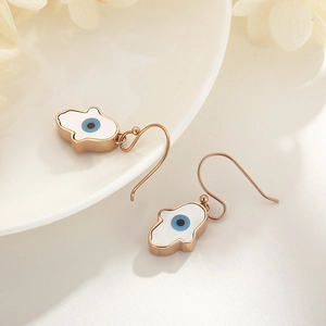 Detail of rose gold Hamsa Hand earrings with Evil Eye hanging on a white ceramic dish