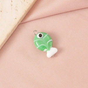 Macro shot of green handmade glass fish pendant with white texture on pink satin