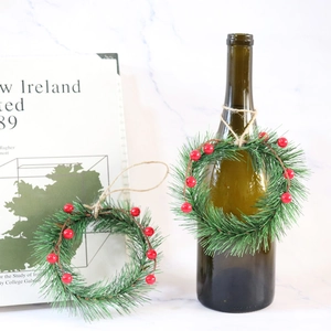 Two-piece Christmas pine needle and red berry wreaths hanging on a green bottle