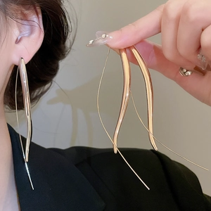 Macro detail of elegant gold-toned long teardrop hook earrings on model with sleek metallic finish