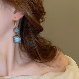 Close-up of vintage blue geometric earrings with gold stripes worn by a model