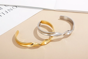 Minimalist twisted open bangle bracelets in gold and silver finish on geometric props