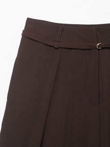 Dettaglio di pantaloni larghi marrone scuro con cintura sottile e fibbia a C dorata