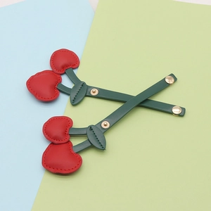 Detail of red cherry PU leather keychain with green leaves and gold metal fastener