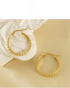 Macro detail of 18K gold titanium steel hoop earrings with elegant spiral texture