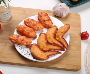 Macro detail of realistic artificial PVC chicken wings on a white ceramic display plate