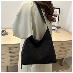 Detail shot of a black suede tote bag worn over the shoulder with minimalist stitching