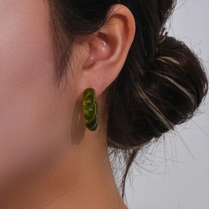 Détail macro de boucles d'oreilles en acrylique vert forêt avec texture torsadée sur modèle