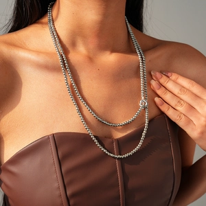 Detail view of a double-layered silver beaded necklace with floral toggle clasp on model