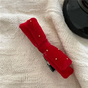 Close-up of red velvet cherry hair clip with gold bead details on beige fabric background
