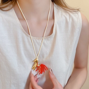 Close-up of golden horse pendant with elegant red beaded tassel on a white woven cord
