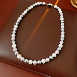 Detailed shot of tricolor pearls on a dark leather base with a silver metal clasp