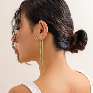 Close-up of golden bow earrings with long tassels worn by a model in a side view